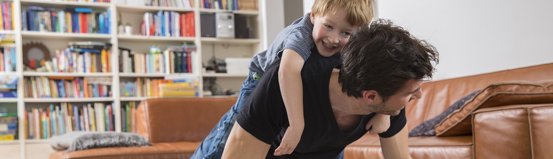 man doing push ups with his son on laughing on his back in the living room