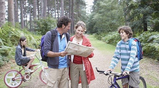 mother and father smiling and reading a map in the woods with their kids on bikes around them